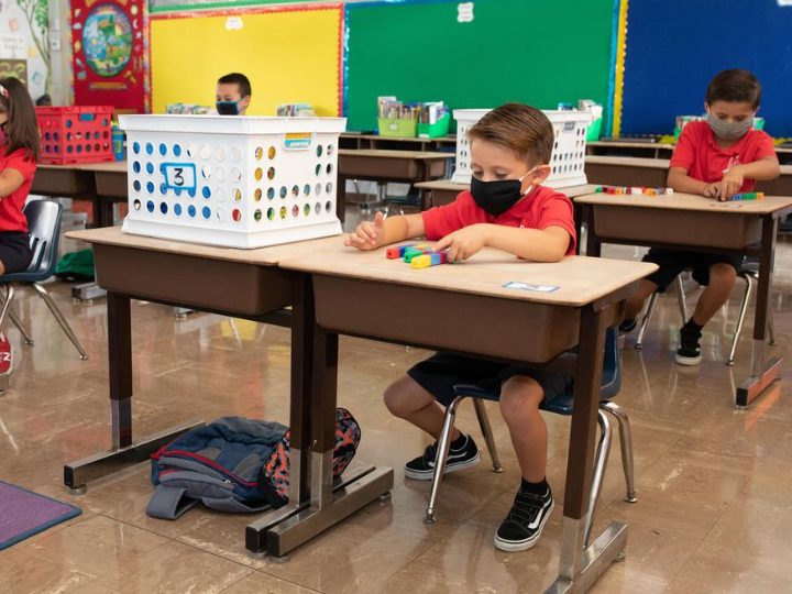 young kids sitting at desks wearing masks